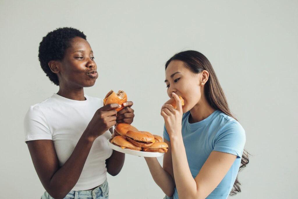 Two women eating burgers while discussing constant hunger and weight loss struggles.